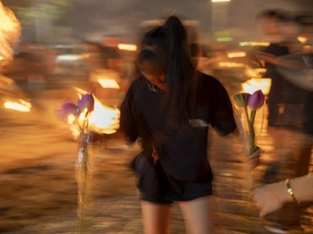 一位年轻女子手持花和蜡烛走在夜晚的街道上