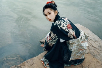 年轻女子穿着日本传统服装坐在河边一块岩石上