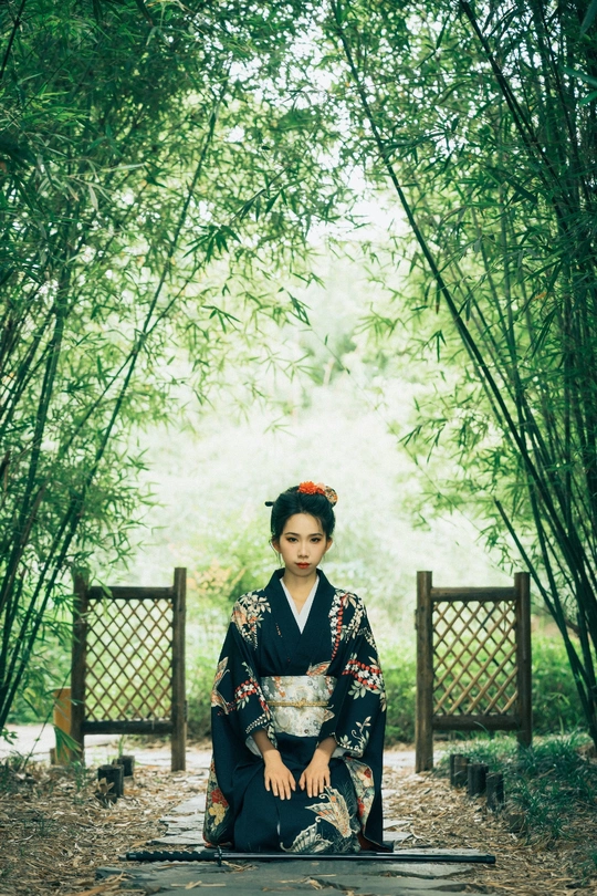 一位年轻女子穿着和服坐在森林中的一块石头小径上