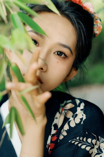 一位穿着和服的年轻女子 手里拿着一束开花的植物枝条 头发上插着花 正对着相机。