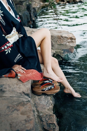 一位穿着连衣裙和拖鞋的女性坐在岩石上 双脚在水中