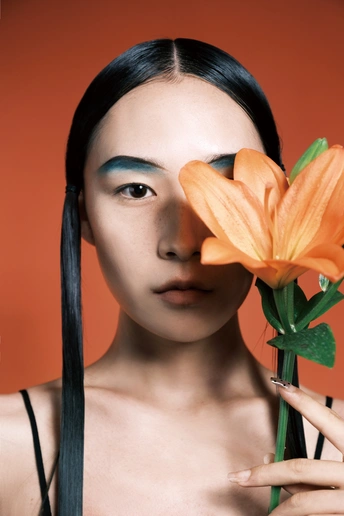 一位长着蓝眼睛、长发飘飘的年轻女子在橙色背景前为肖像画摆姿势 背景中有橙色花朵。