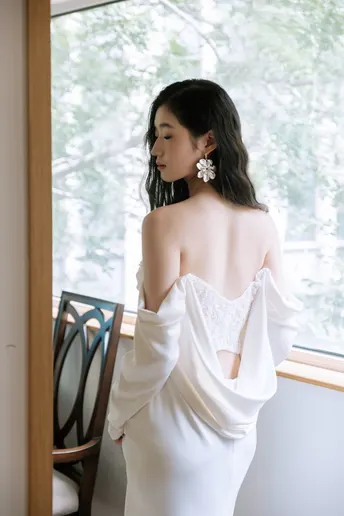 新娘穿着一件白色婚纱站在窗户前