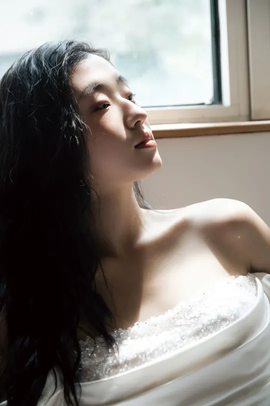一位穿着白色连衣裙的年轻女子正在窗户旁向外看