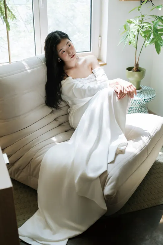 一位穿着白色长袍的女人坐在白色沙发上 面对窗户。