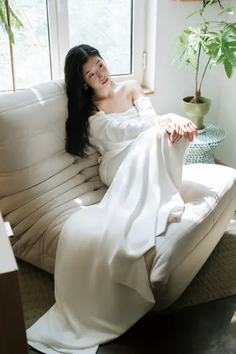 一位穿着白色长袍的女人坐在白色沙发上 面对窗户。