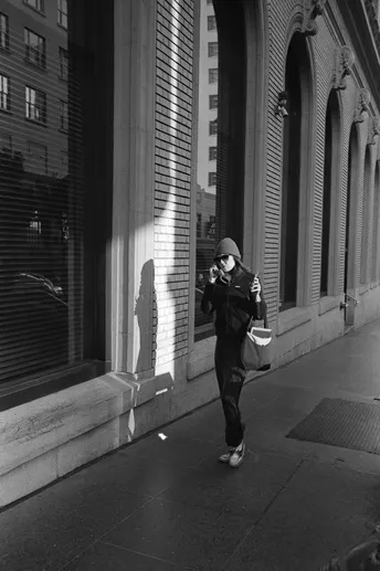 一位妇女走在人行道上 边打电话边拿着一个包 站在一栋建筑前。