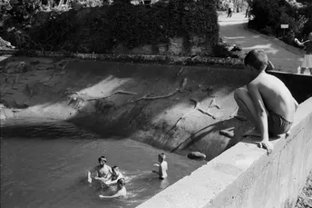 一个黑白照片 一个站在墙上的人正在观看一个在水中玩耍的年轻男孩。