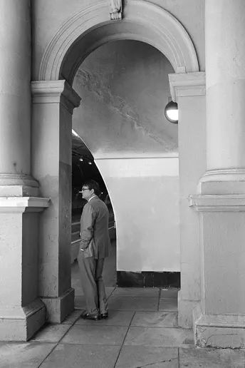 一张黑白照片 一位穿西装的男子站在一栋建筑的入口处。