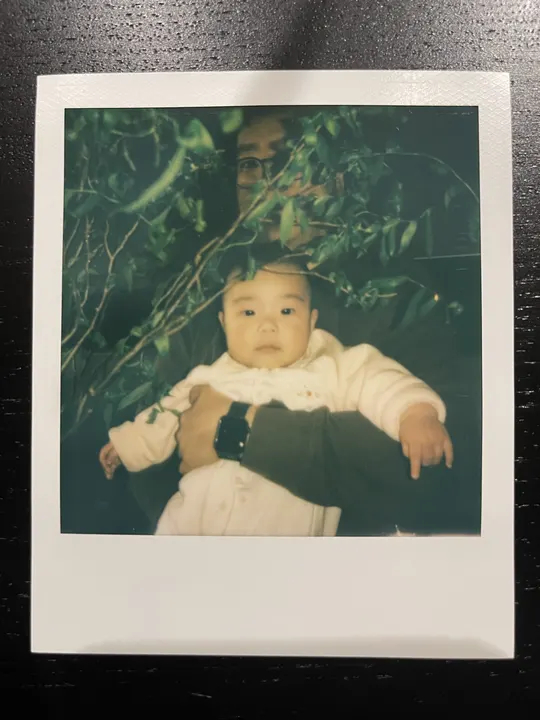 一张老黑白照片 一个年轻男孩抱着一个小孩子 站在一棵树旁边。