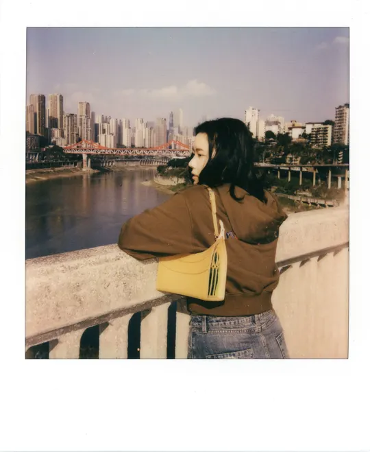 站在水上桥梁上的黄色包的女人的