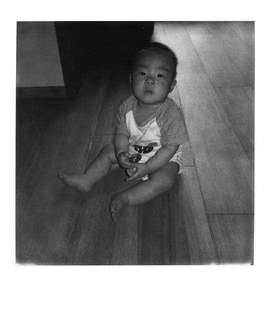 一张黑白照片 一个小男孩坐在地板上的一所房子里