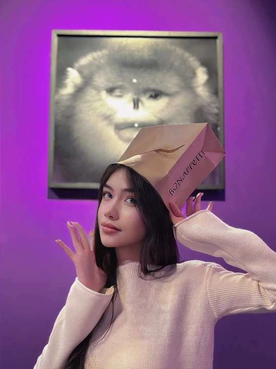 一位年轻女子举着粉红色纸袋在头上与一只猫合影