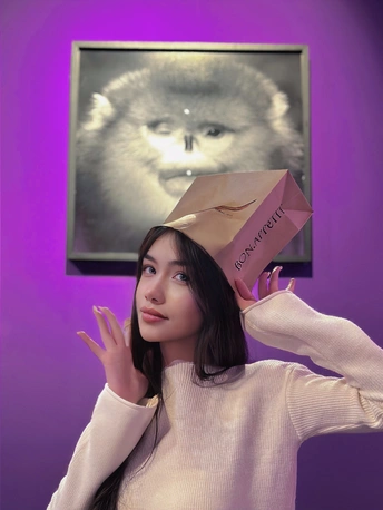 一位年轻女子举着粉红色纸袋在头上与一只猫合影