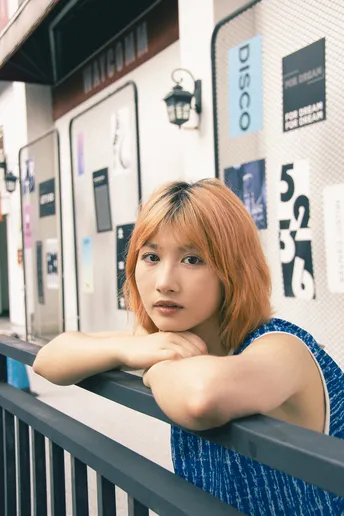 一位红发女子穿着蓝色裙子 倚靠在售卖机前的围栏上