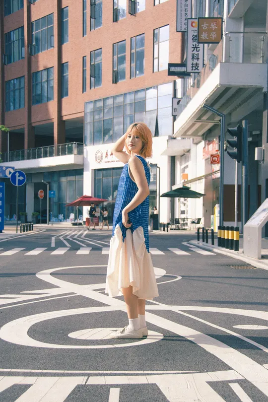 一位穿着蓝白色连衣裙的年轻女子穿越城市街道的人行横道。