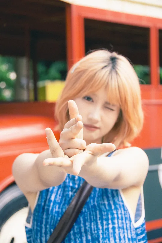 一位年轻女子举起双手 用大拇指向上指着相机 手指在红色公交车前做出一个手势。