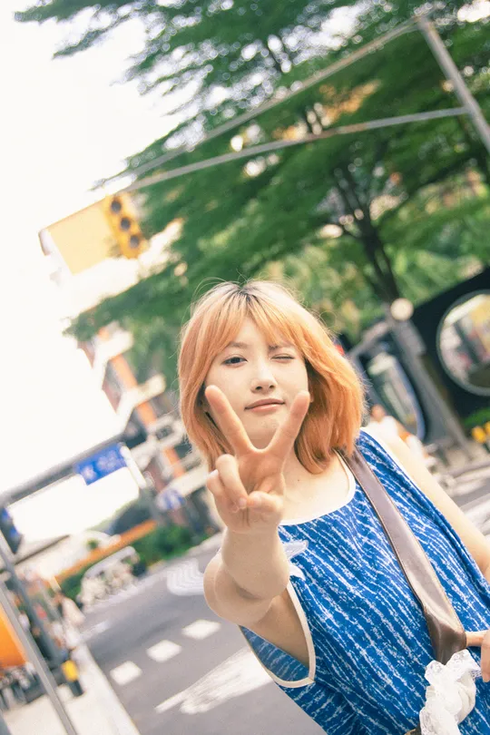 一位穿着蓝色的年轻女子举起她的手 手指指向她脸颊的侧面 并指向相机。