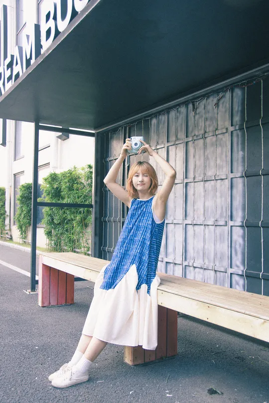 一位穿着蓝白色连衣裙的年轻女子坐在靠近建筑的木凳上