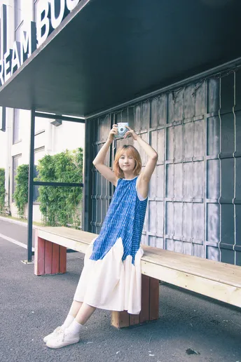 一位穿着蓝白色连衣裙的年轻女子坐在靠近建筑的木凳上