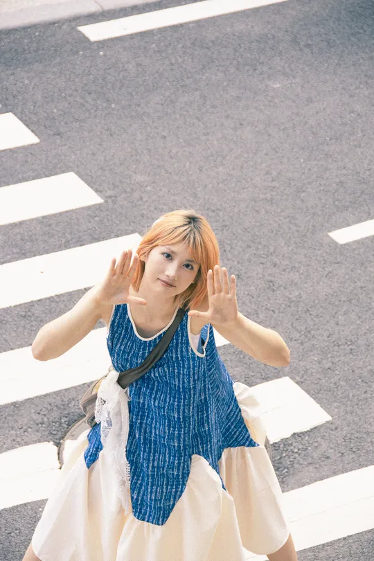 一位穿着连衣裙的年轻女子在人行横道上过马路时举起双手。