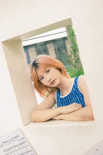 一位穿着蓝色衣服的年轻女子靠在一面镜子上 正在凝视窗外。