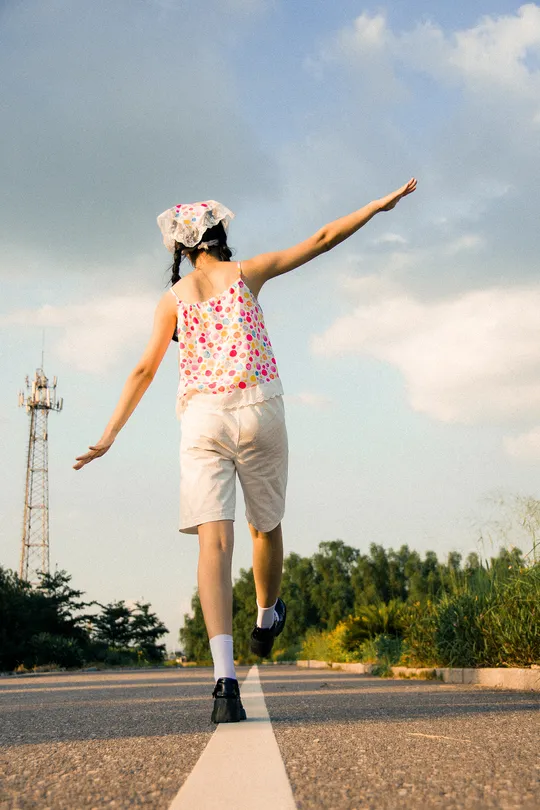 一个小女孩在公路中央骑着滑板 张开双臂在空中跳跃。