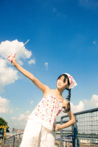 一位穿着连衣裙的年轻女子伸开双臂 一只风筝在蔚蓝的天空中飞翔。