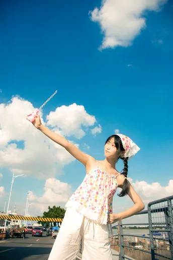 一位年轻女子站在停车场 在蓝天下放飞风筝。