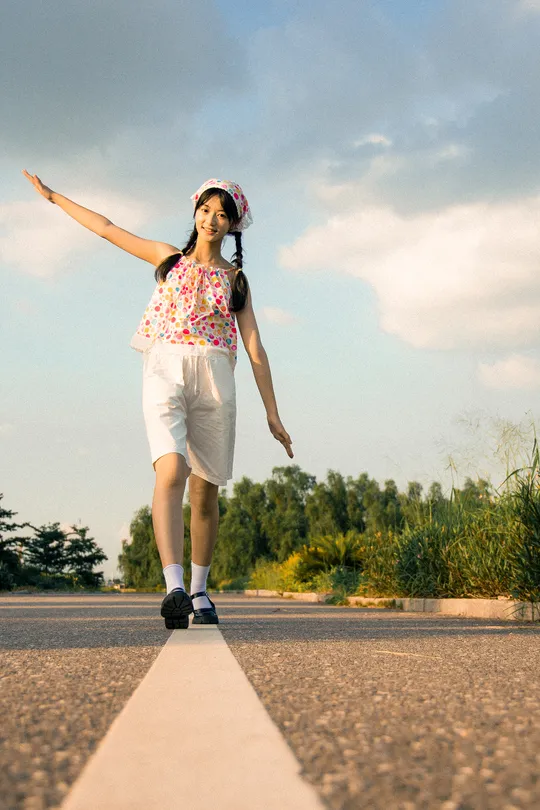 一个女孩站在一辆空置的滑板车上 位于空旷的道路上。
