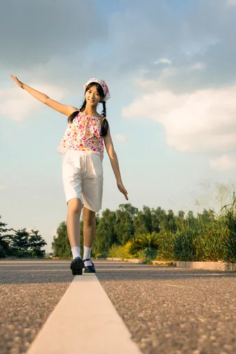 一个女孩站在一辆空置的滑板车上 位于空旷的道路上。