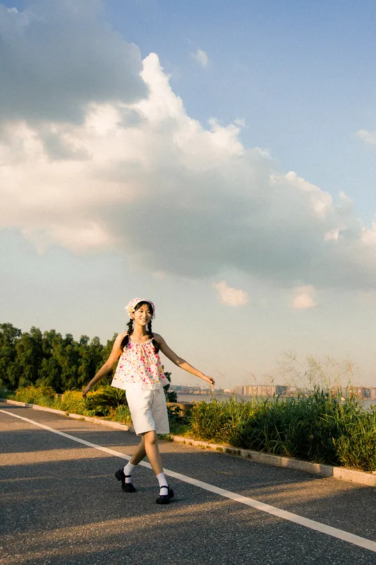 一个穿着连衣裙的年轻女子 手里拿着滑板 走在一条空荡荡的路上。