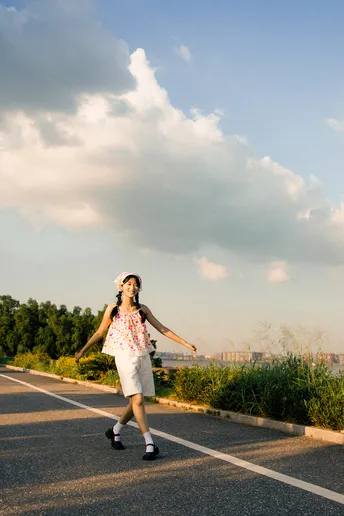 一个穿着连衣裙的年轻女子 手里拿着滑板 走在一条空荡荡的路上。