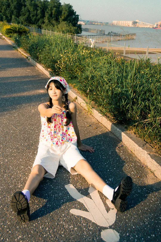 一个年轻女孩坐在滑板上 在街道的角落里 靠近水边摆姿势。