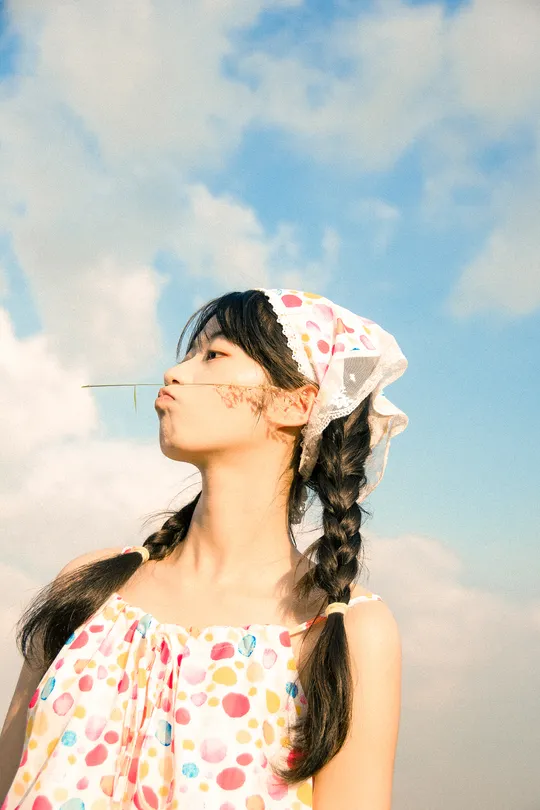 一位穿着花裙子的年轻女子站在多云的蓝色天空中 从口中吹出气泡。