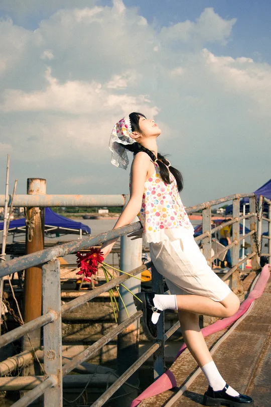 一位穿着连衣裙的年轻女子沿着有花盆的码头在水边走