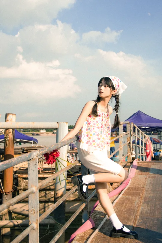 一个穿粉色连衣裙的年轻女子坐在码头附近的防波堤上