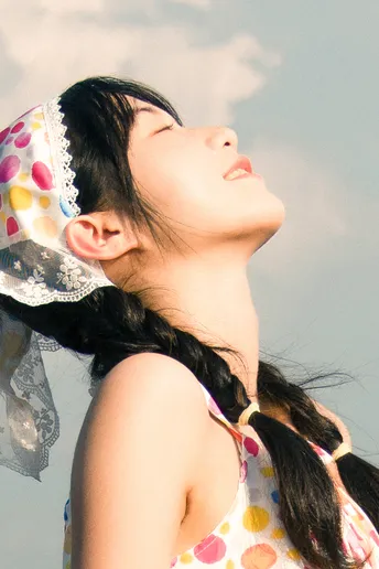 一个闭着眼睛仰望着阴沉的蓝天上飘着云的女孩 头顶上方有云。