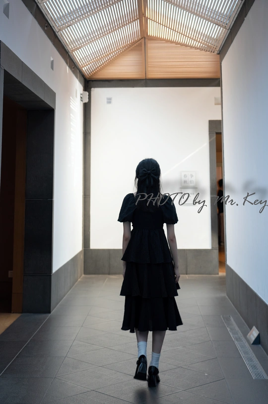 一位穿着黑色连衣裙的年轻女子正在一栋建筑物的走廊里走动。