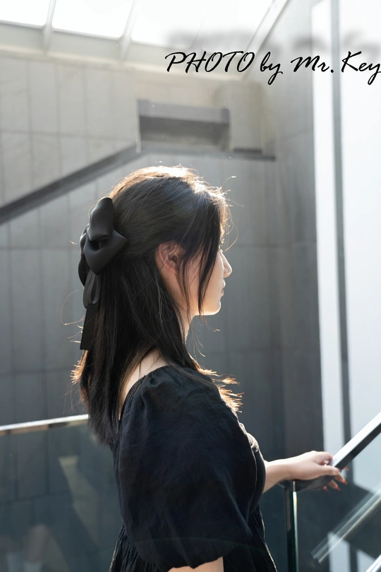 一个穿着黑色连衣裙 头戴蝴蝶结的年轻女子站在一个自动扶梯上。