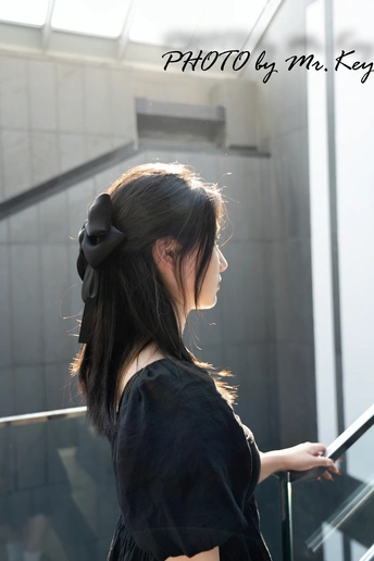 一个穿着黑色连衣裙 头戴蝴蝶结的年轻女子站在一个自动扶梯上。