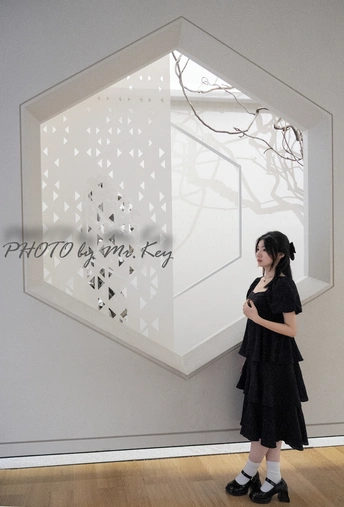 一位穿着黑白衣服的年轻女子站在一个房间 墙上挂有一幅画。