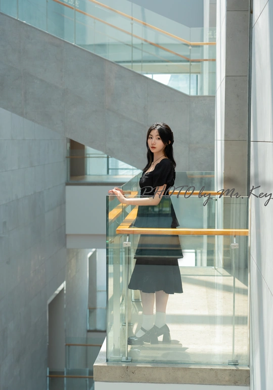 一个穿着黑色连衣裙的年轻女子站在一座现代办公楼的楼梯上