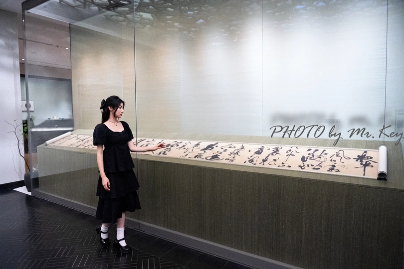 一位穿着黑色连衣裙的女人站在一面墙前