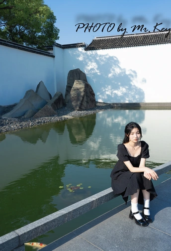一张年轻女子穿着黑色连衣裙坐在池塘边上 水中有鱼。
