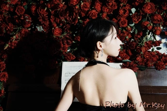 一个穿着黑色连衣裙的年轻女子坐在红玫瑰墙前