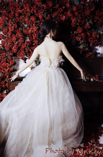 一位身着白色长裙的模特 站在红色的花丛前