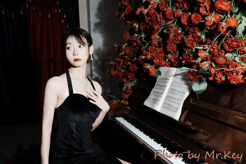 一个穿着黑色连衣裙的年轻女子坐在红玫瑰前的钢琴前