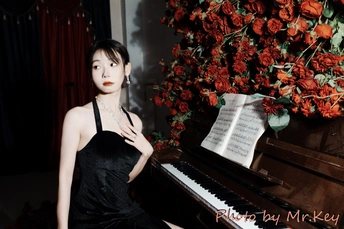 一个穿着黑色连衣裙的年轻女子坐在红玫瑰前的钢琴前