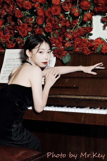 一位穿着黑色连衣裙的年轻女子在红玫瑰前弹钢琴